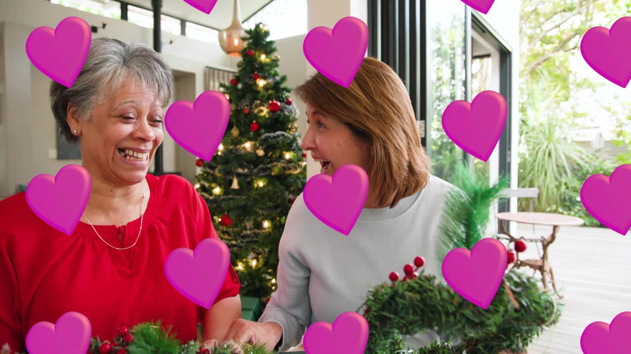 Two women assembling wreaths for holiday decor picking twine tucking berries pink hearts overlaying