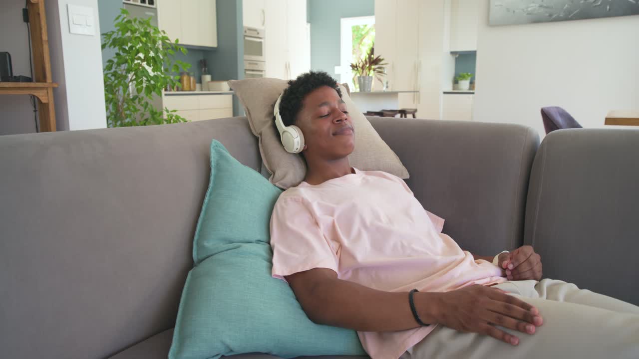 La telecamera si avvicina, un uomo afroamericano è sdraiato sul divano con le cuffie e ascolta a casa.
