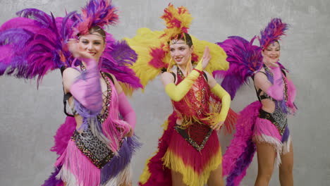 grupo de artistas femeninas en vestidos de plumas bailando y moviendo sus manos de lado a lado