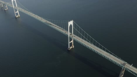 Drone-shot-of-a-big-bridge-that-crosses-the-water,-moving-to-the-right-and-slowly-tilting-down