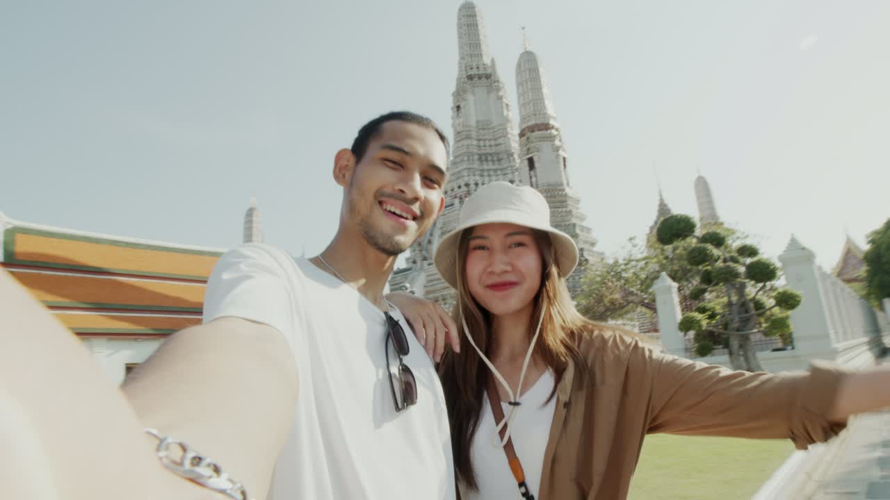 una pareja de turistas asiáticos felices se toman selfies y hacen una llamada de video en wat arun en tailandia.