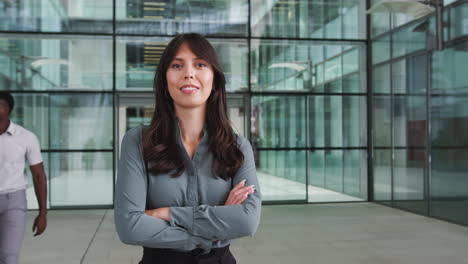 Portrait-Of-Businesswoman-Standing-In-Lobby-Of-Busy-Modern-Office