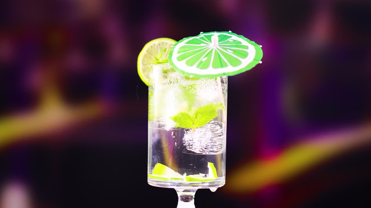 A mojito cocktail garnished with lime and mint, set against a colorful, blurred background with dynamic lighting