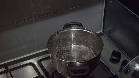 caucasian hand lifts lid on cook pot of hot water on gas stove burner