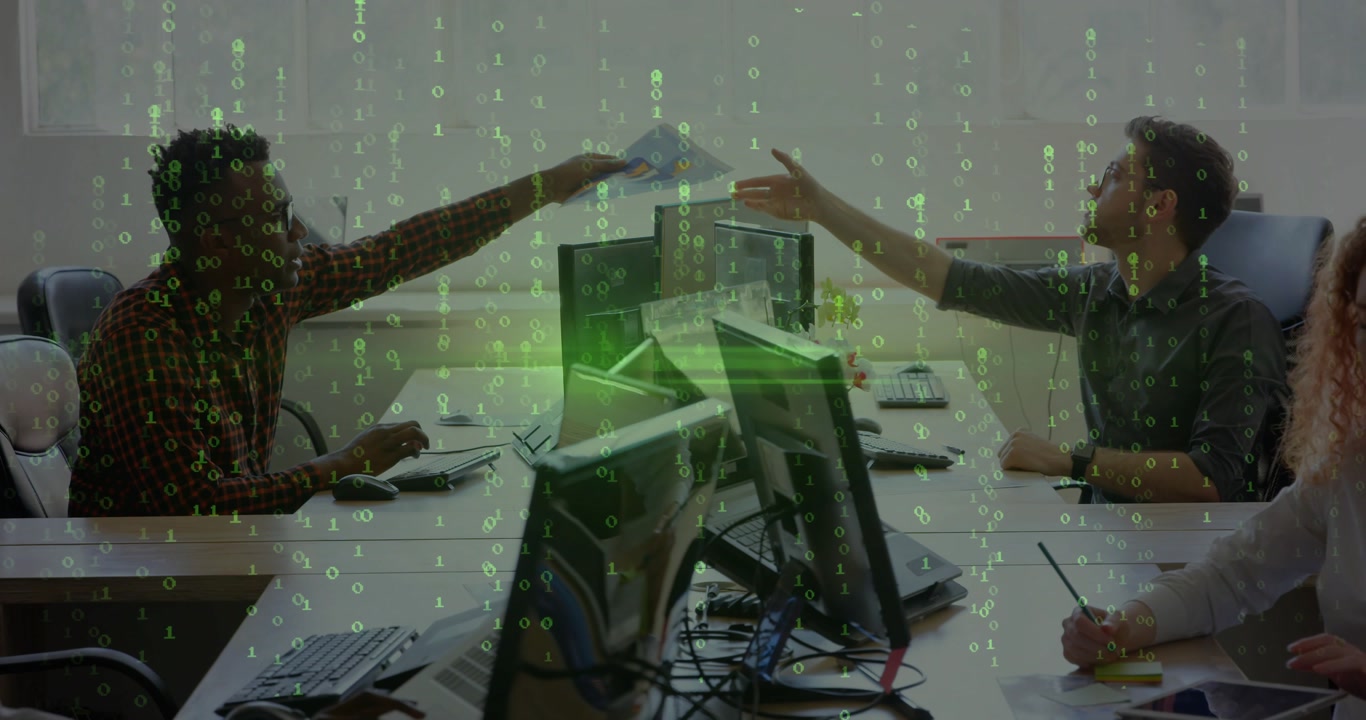 Left office staff handing paper causing peer reaching over screens to check; green overlay on hands