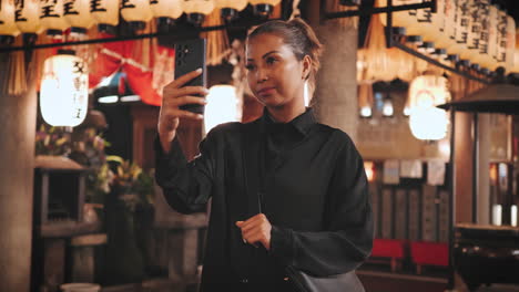 Contemplative-woman-in-black-stands-with-her-smartphone-at-a-Japanese-shrine