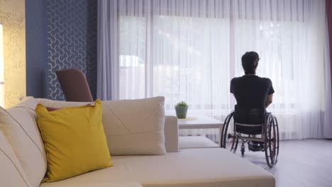 joven sentado en silla de ruedas caminando por la casa y mirando por la ventana.