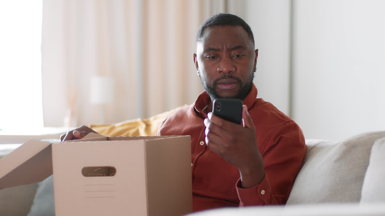 Man unpacking a box on a couch using a phone