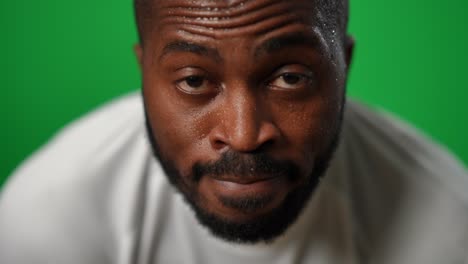 vista frontal de un confiado deportista afroamericano sudoroso mirando a la cámara en el fondo de chromakey. hombre concentrado sudoroso posando en la pantalla verde con una expresión facial seria.