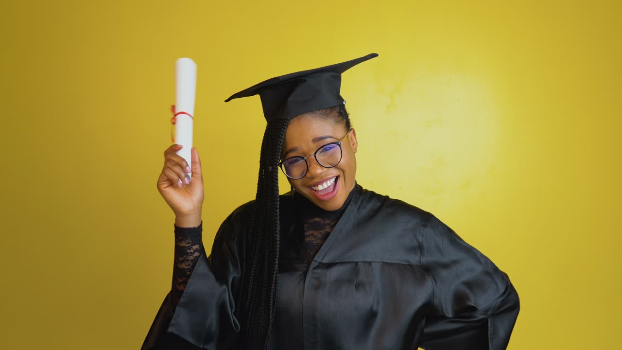 un estudiante de posgrado alegre tiene un diploma internacional y expresa felicidad y emociones positivas. estudiante con una túnica negra y sombrero sobre un fondo amarillo mira a la cámara. proceso de bologna