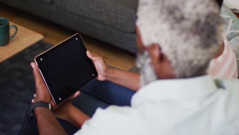 African-american-senior-man-sitting-on-sofa-making-video-call-using-tablet