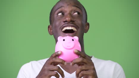 young happy african man looking surprised while holding piggy bank