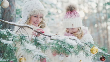 a little girl and a young mother decorate a christmas tree with decorative balls in the snow-covered