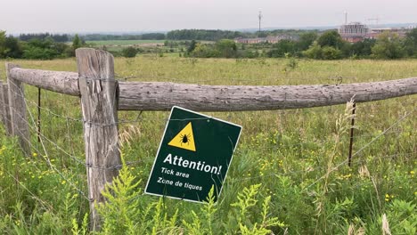 tick area warning sign on rural park trail fence with tall grass in farmland field