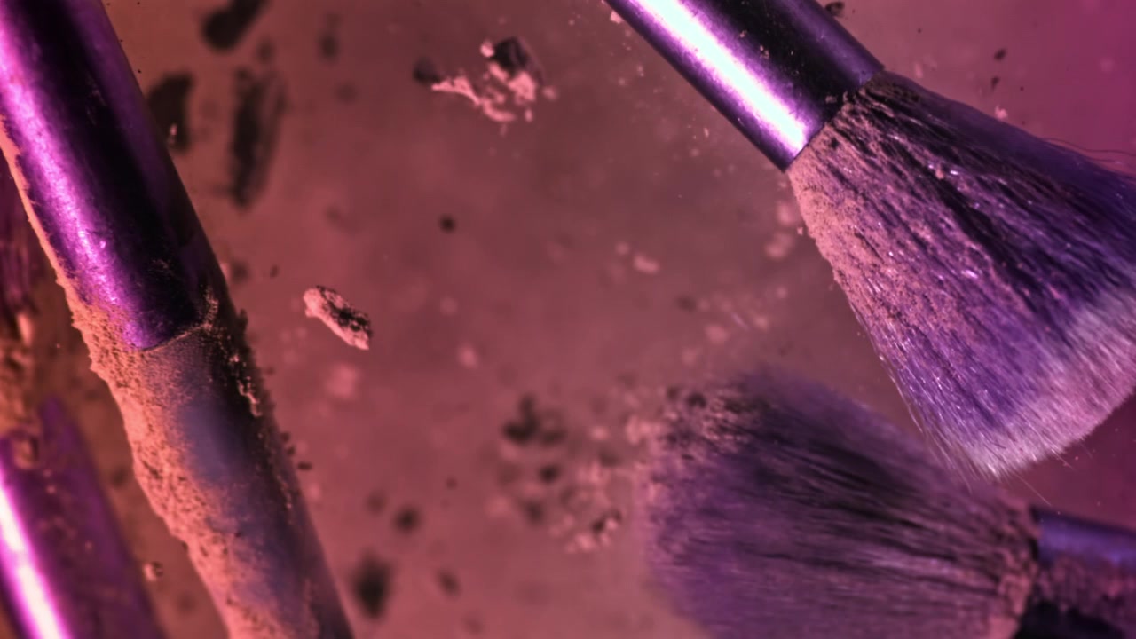 Makeup Brushes Releasing Powder Particles in Pink and Purple Liquid
