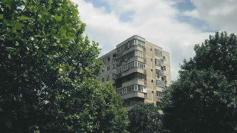 pan right shot with a block of flats framed by trees with green leaves, somewhere in eastern europe