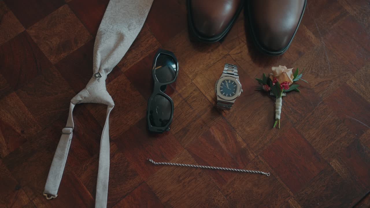 Flat lay of groom shoes tie watch sunglasses and boutonniere