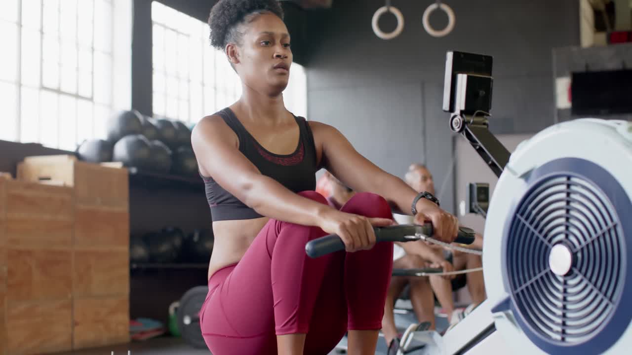 Donna afroamericana concentrata che si allena su un vogatore in palestra, al rallentatore.