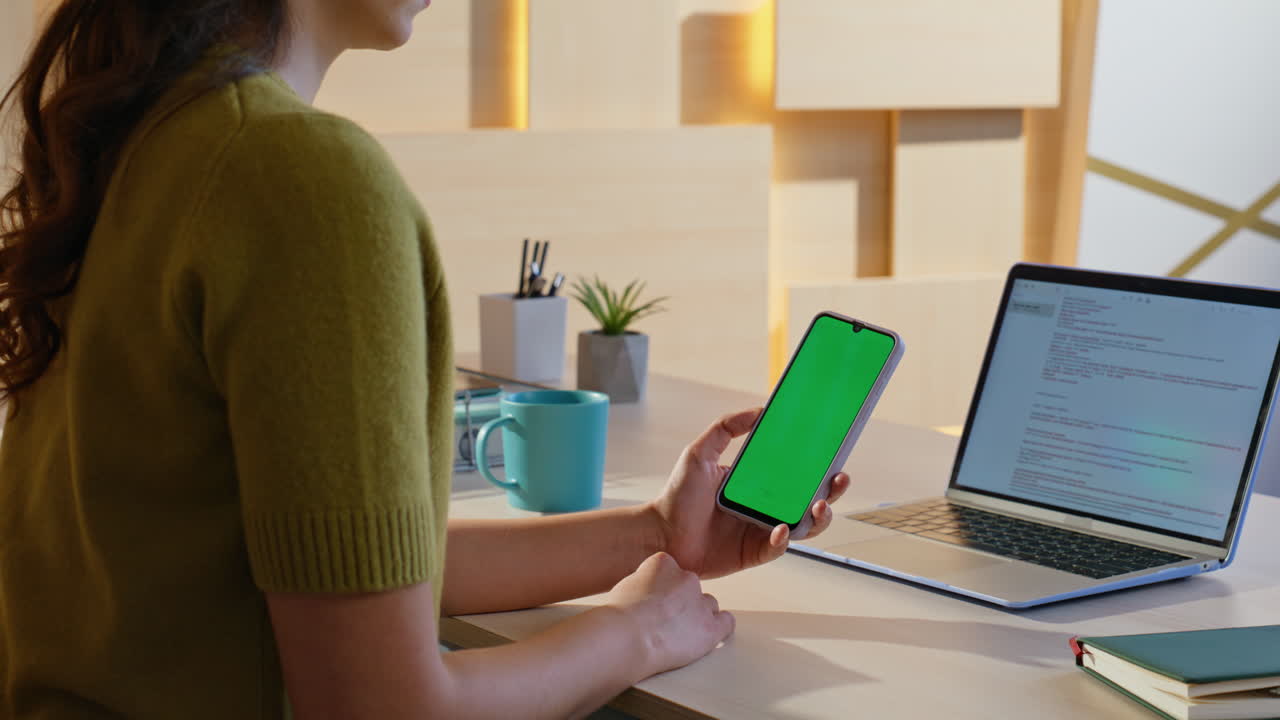 Woman using smartphone with green screen at her desk