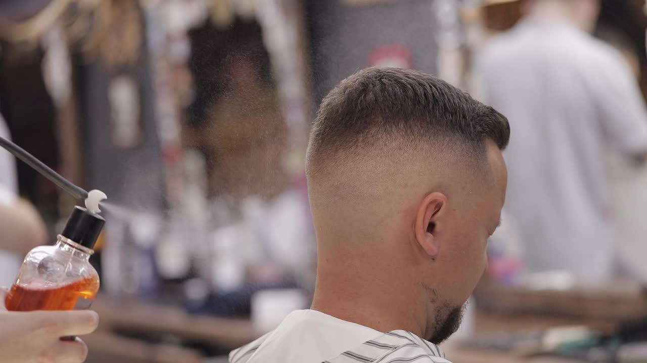 barbero pulveriza perfume de la botella en el cabello del cliente, barbero hace corte de pelo para el novio en la barbería