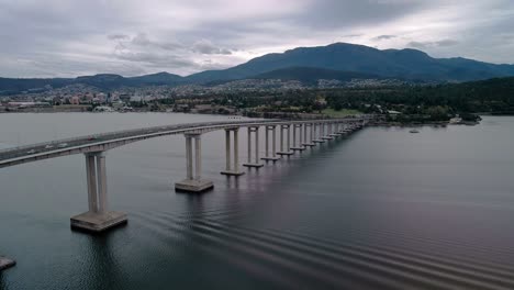 parallax aerial view of a bridge with cars running on it during sunset with cityscape at background