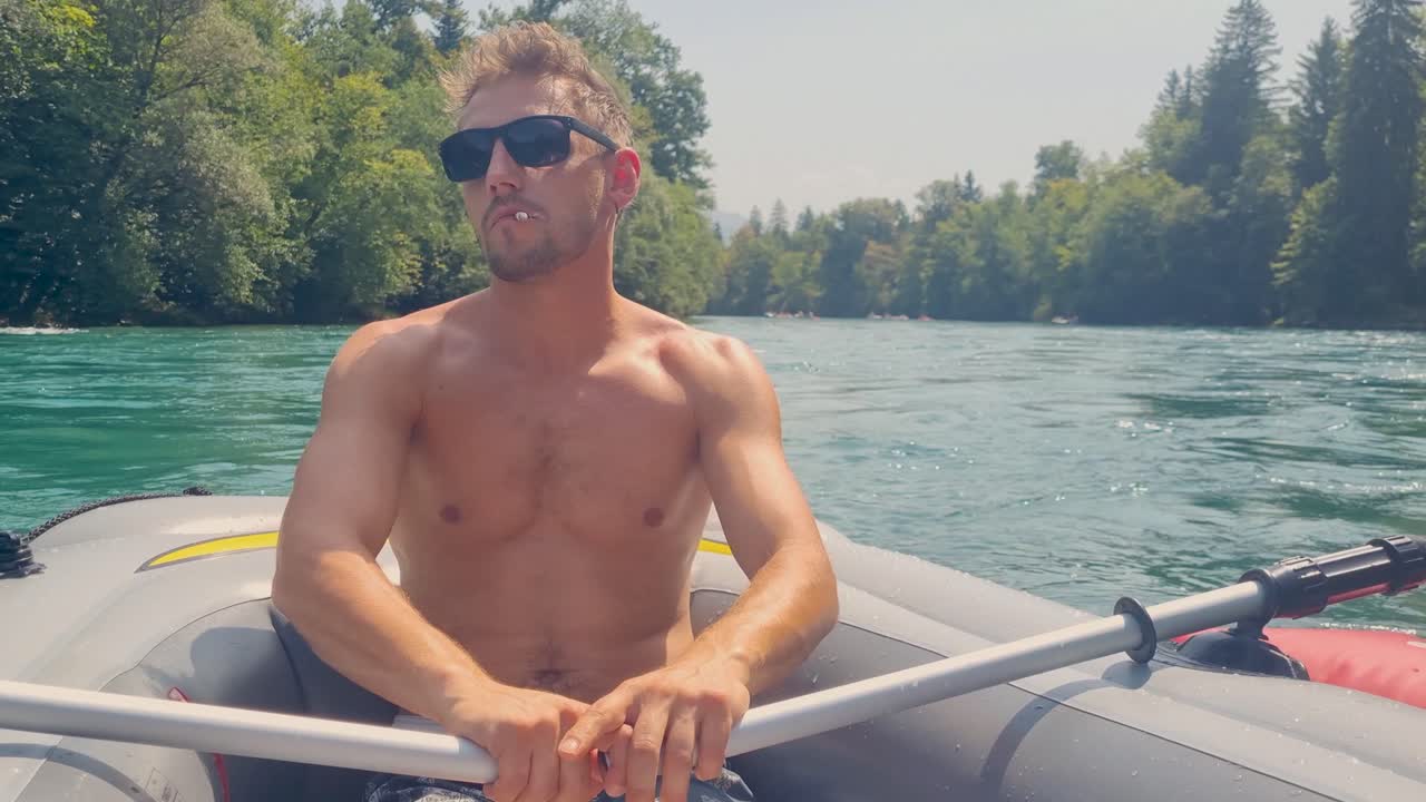 Attractive man with sunglasses and cigarette paddles an inflatable boat on turquoise Aare River in Bern, Switzerland, enjoying a sunny summer day and popular local activity