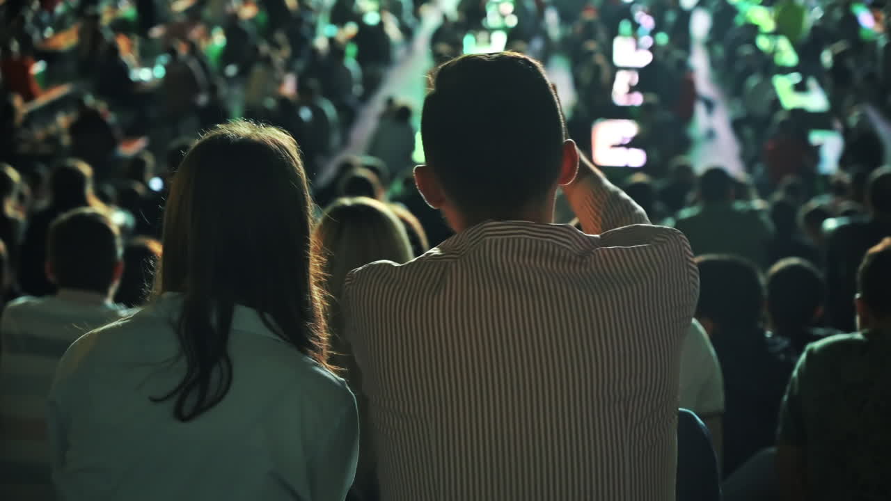 Sitting couple watching football in a public place and talking at night