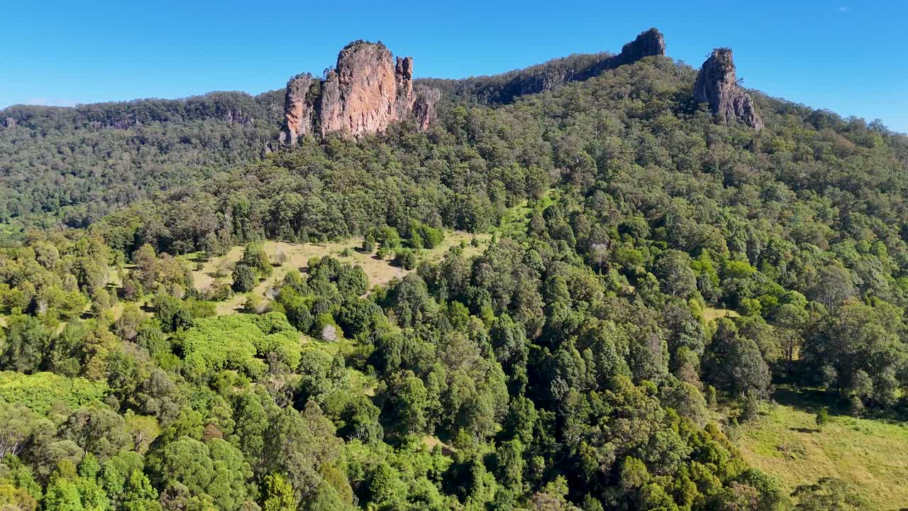 Drone footage captures the lush greenery and striking rhyolite volcanic plugs of Nimbin Rocks under clear blue skies