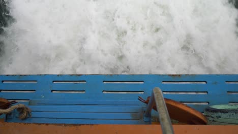 overhead of a ferry boat cutting through ocean waters, churning waves visible below. high angle shot