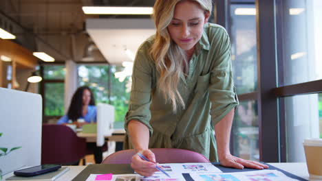 mature businesswoman standing at desk in office approving or checking proofs or design layouts