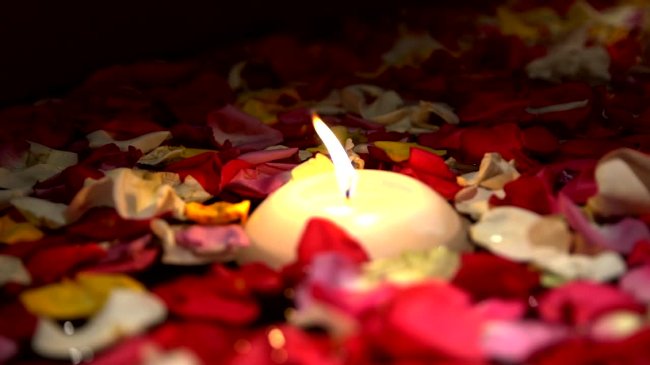 vela romántica en cámara lenta con llama parpadeante flotando en los pétalos de las flores