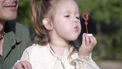 a cheerful little girl playing with the bubbles with her father in the park