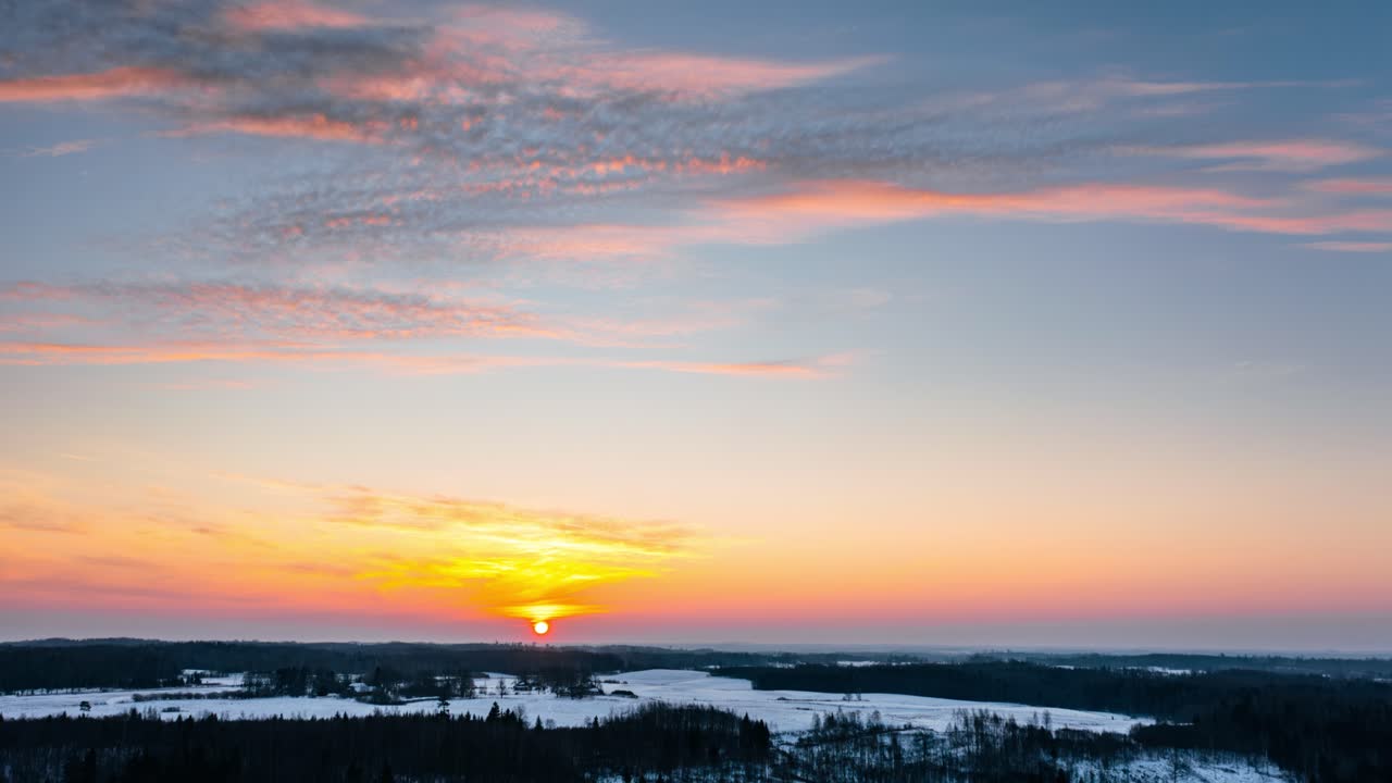 Stunning winter sunrise over snow covered forest in countryside landscape. Aerial drone hyperlapse of sunrise over the horizon.