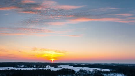 stunning winter sunrise over snow covered forest in countryside landscape. aerial drone hyperlapse of sunrise over the horizon.