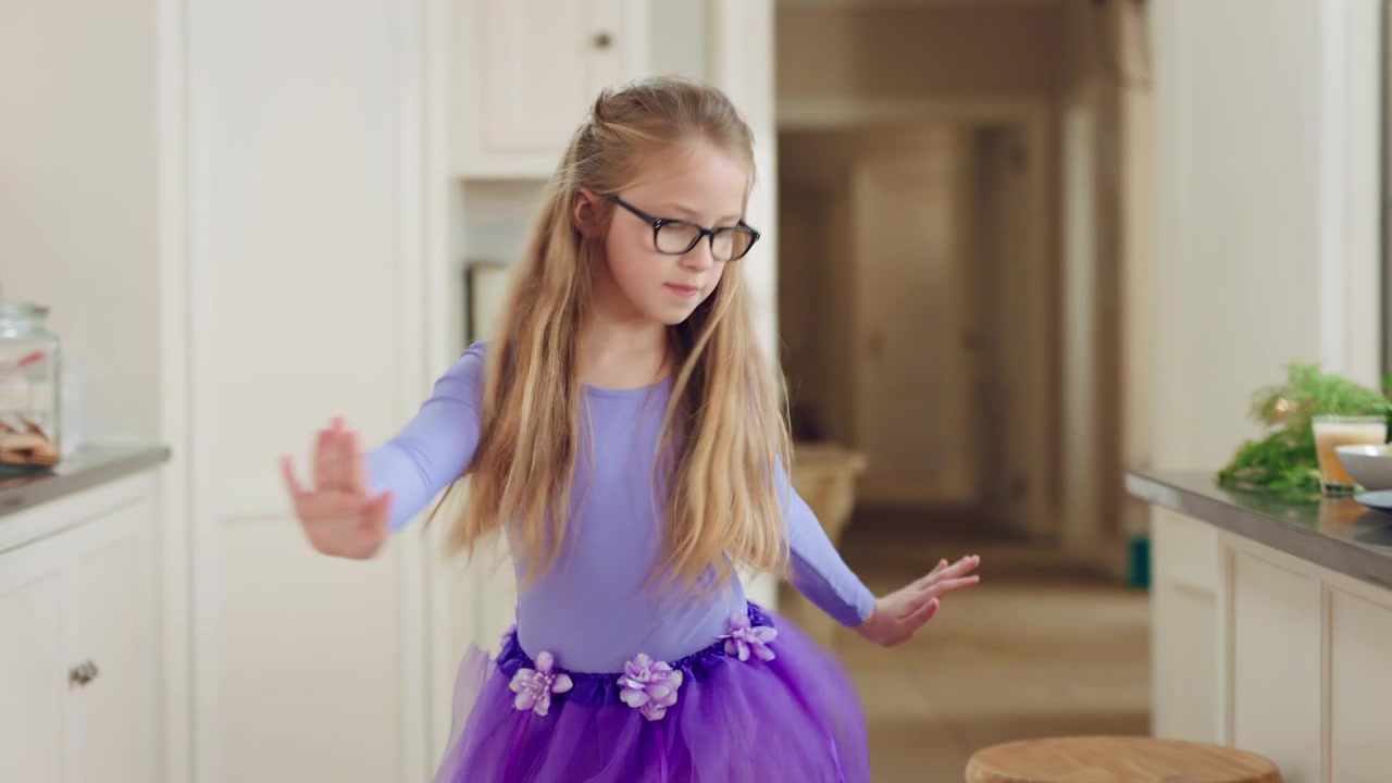 Bambina che balla con un tutù viola in cucina