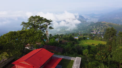 Aerial-establishing-shot-showing-colorful-houses-on-slope-of-mountain-in-Nepal-with-beautiful-with-into-cloudy-valley---Top-down-forward-flight