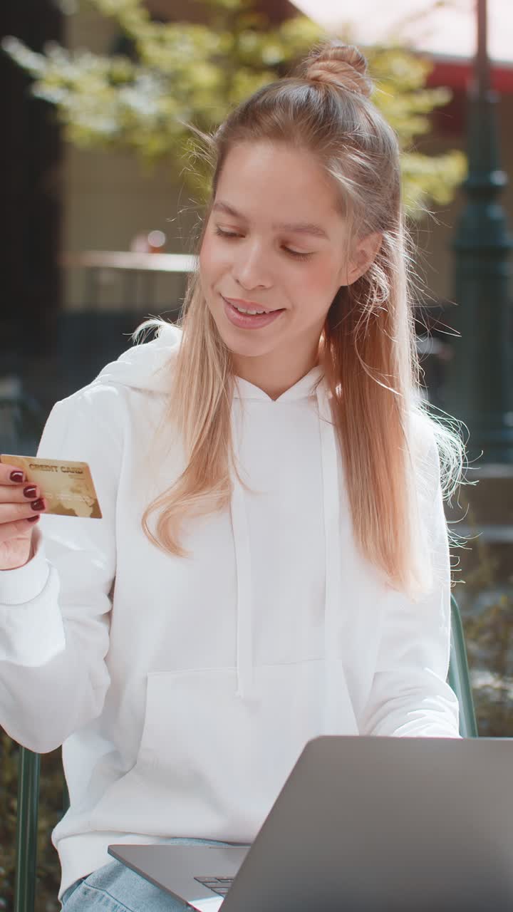 Happy young woman girl using credit bank card and laptop purchases online shopping on city street