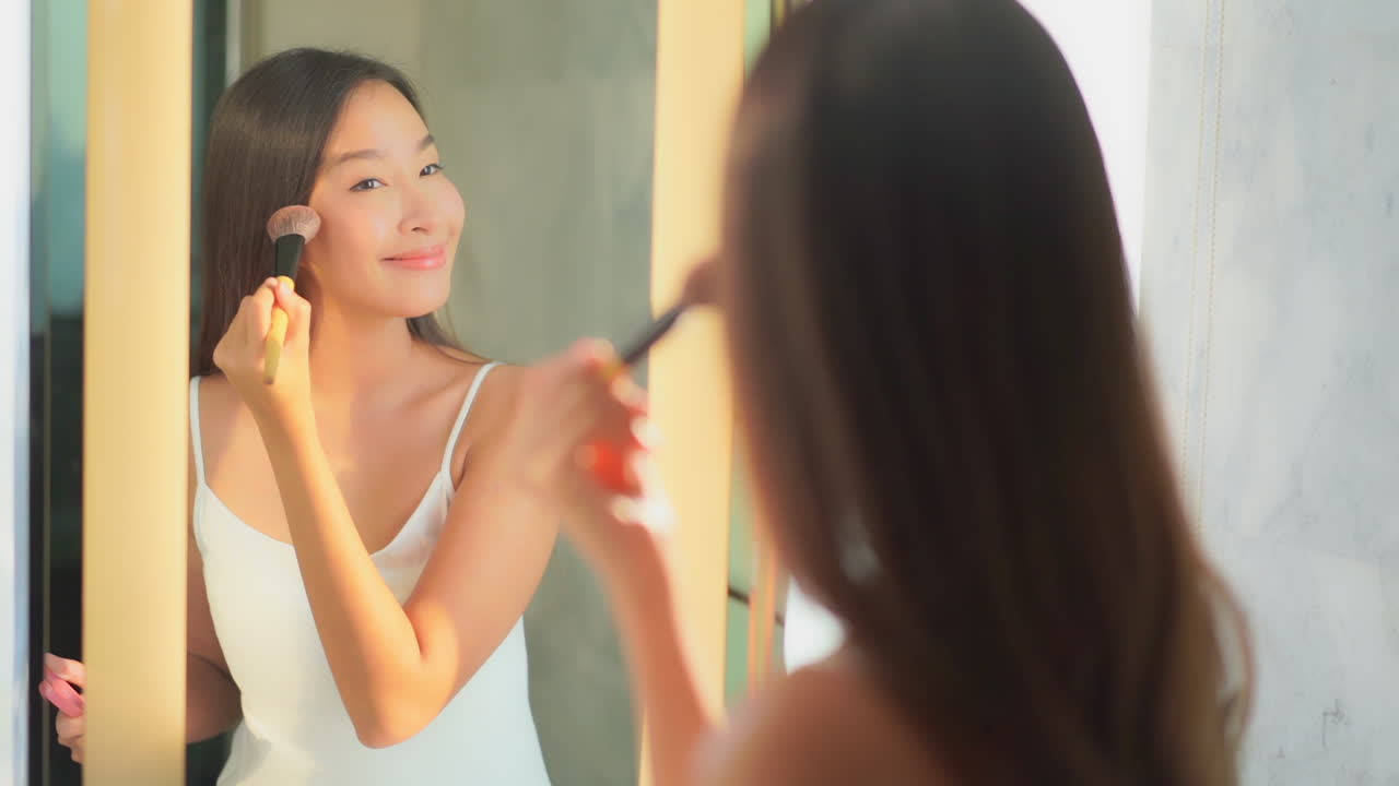 Beautiful Asian woman applying cover-up loose powder to her cheeks with a makeup brush, apply rouge reflection in the mirror