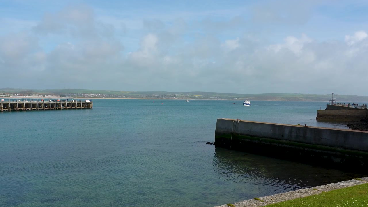 Un'ampia inquadratura panoramica dell'ingresso del porto di Weymouth con il molo in pietra e le calme acque blu, adatta per contenuti di viaggio e turismo