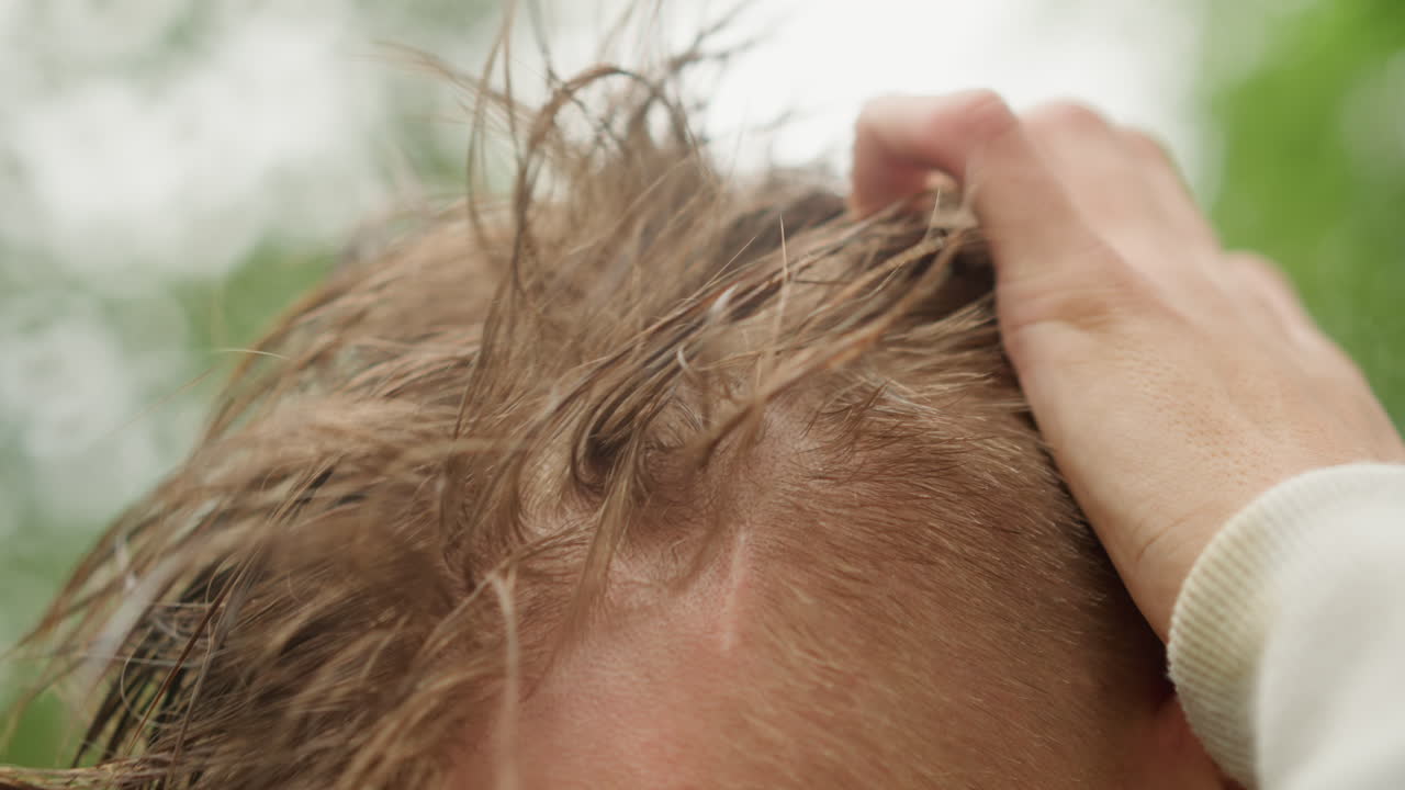 젖은 두피를 부드럽게 만지는 백인 남성의 손, 머리카락을 마사지하고 매만지는 손의 움직임, 흩뿌려지는 물방울, 촉촉한 질감, 차분한 동작, 폭풍 후 손질 루틴, 초록색 잎사귀 배경