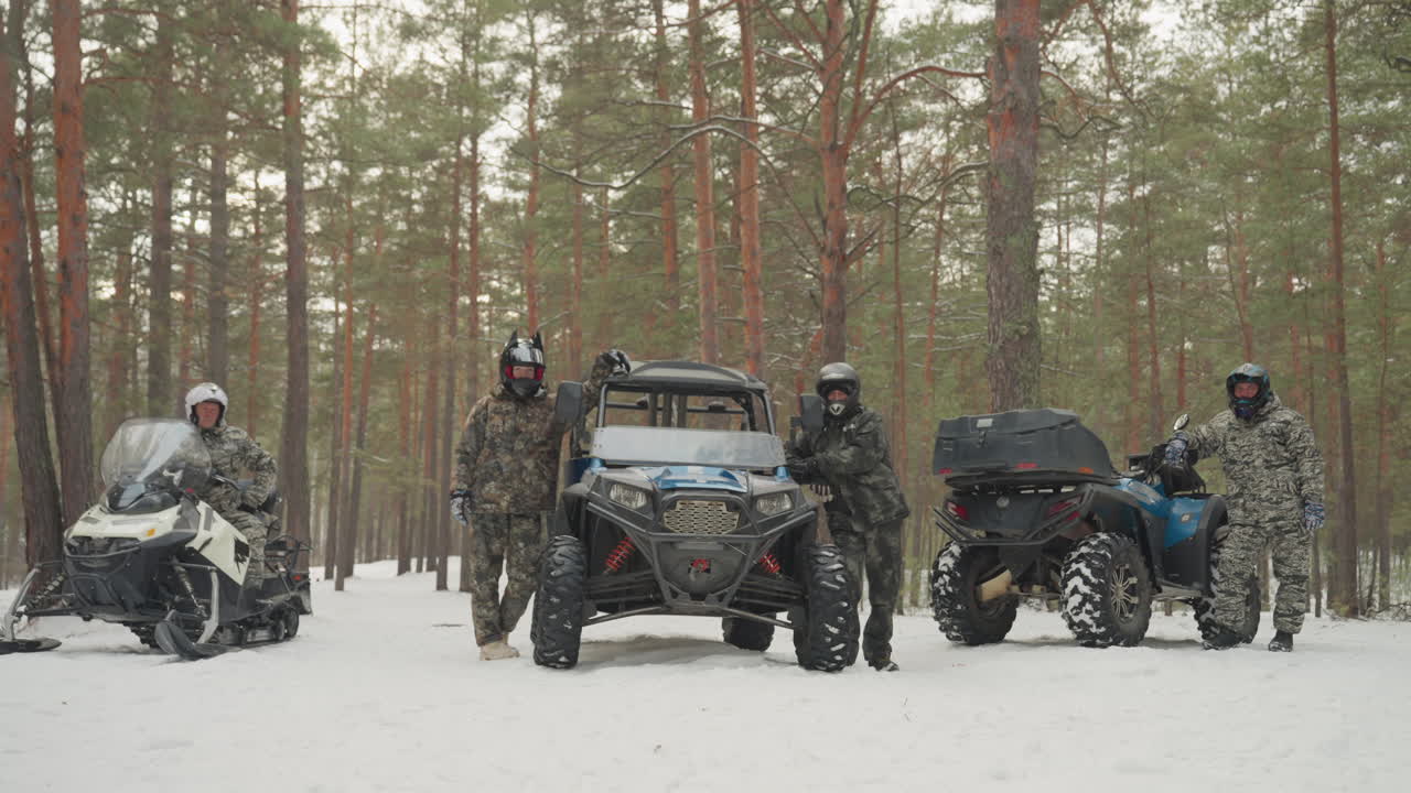 Schieramento di ATV nella foresta innevata con piloti pronti per il rally. Convoglio misto di UTV blu, ATV nero e quad rosso vivo, con i caschi, piloti in mimetica e abbigliamento invernale, sfondo di pini e neve compatta, acceleratore.