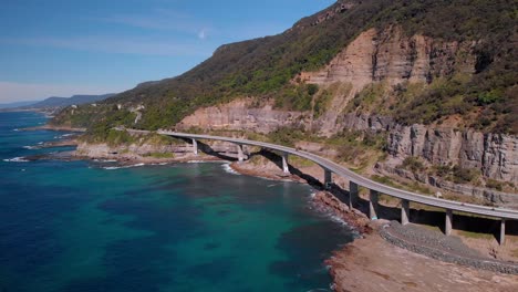 aerial view of sea cliff bridge, sunny day, grand pacific drive, new south wales, australia - backward wide drone shot