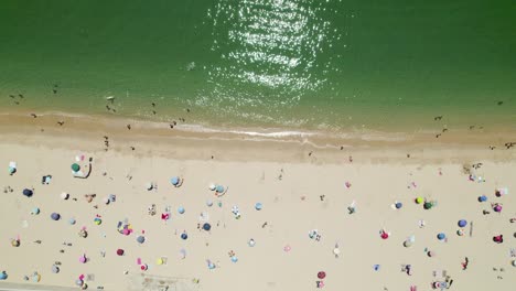 Vista-Aérea-De-Arriba-Hacia-Abajo-A-Lo-Largo-De-Una-Hermosa-Playa-De-Arena,-Agua-Verde-Y-Sombrillas-Coloridas