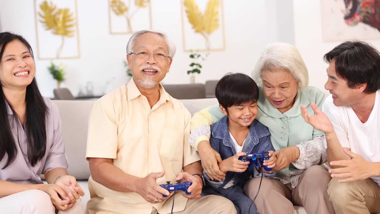 明るく居心地の良いリビングで、多世代のアジア系の家族が一緒に笑いながらビデオゲームをしている様子
