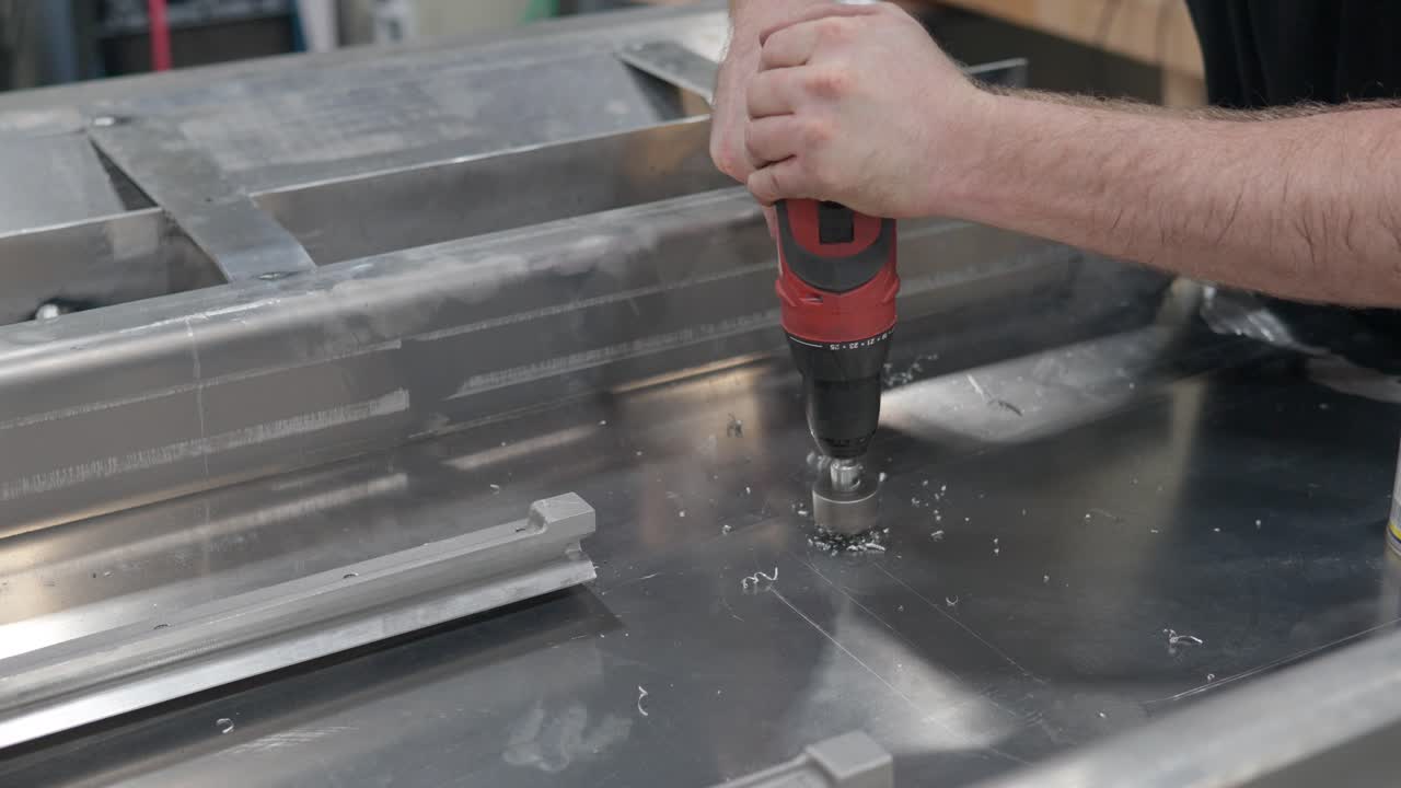 Primer plano de un trabajador presionando un taladro para hacer un agujero en chapa de metal en el estudio