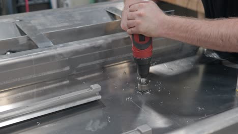 Close-up-of-worker-pushing-on-a-drill-to-make-a-hole-in-metal-sheet-in-studio