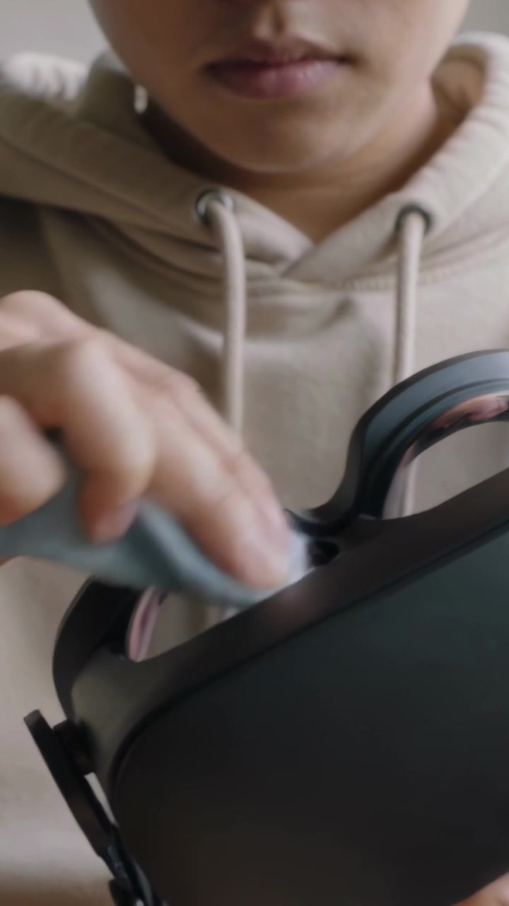 Vertical video: Wiping boy cleaning VR headset in room after grabbing cloth for lenses, in hoodie