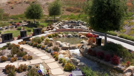 Aerial-close-up-shot-flying-over-a-soothing-waterfall-in-a-nature-garden-at-a-mortuary-in-California