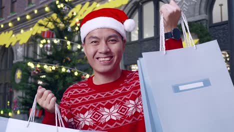 close up of asian man in christmas suit with the shopping bags smiling to the camera while standing in christmas night