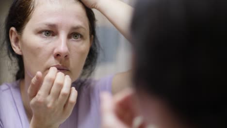 woman confused about facial wrinkles aging skin on forehead looking at mirror. wrinkles on eyes on face skin. woman having problem with eyes bags dark circles wrinkles. stress depression fatigue diet.